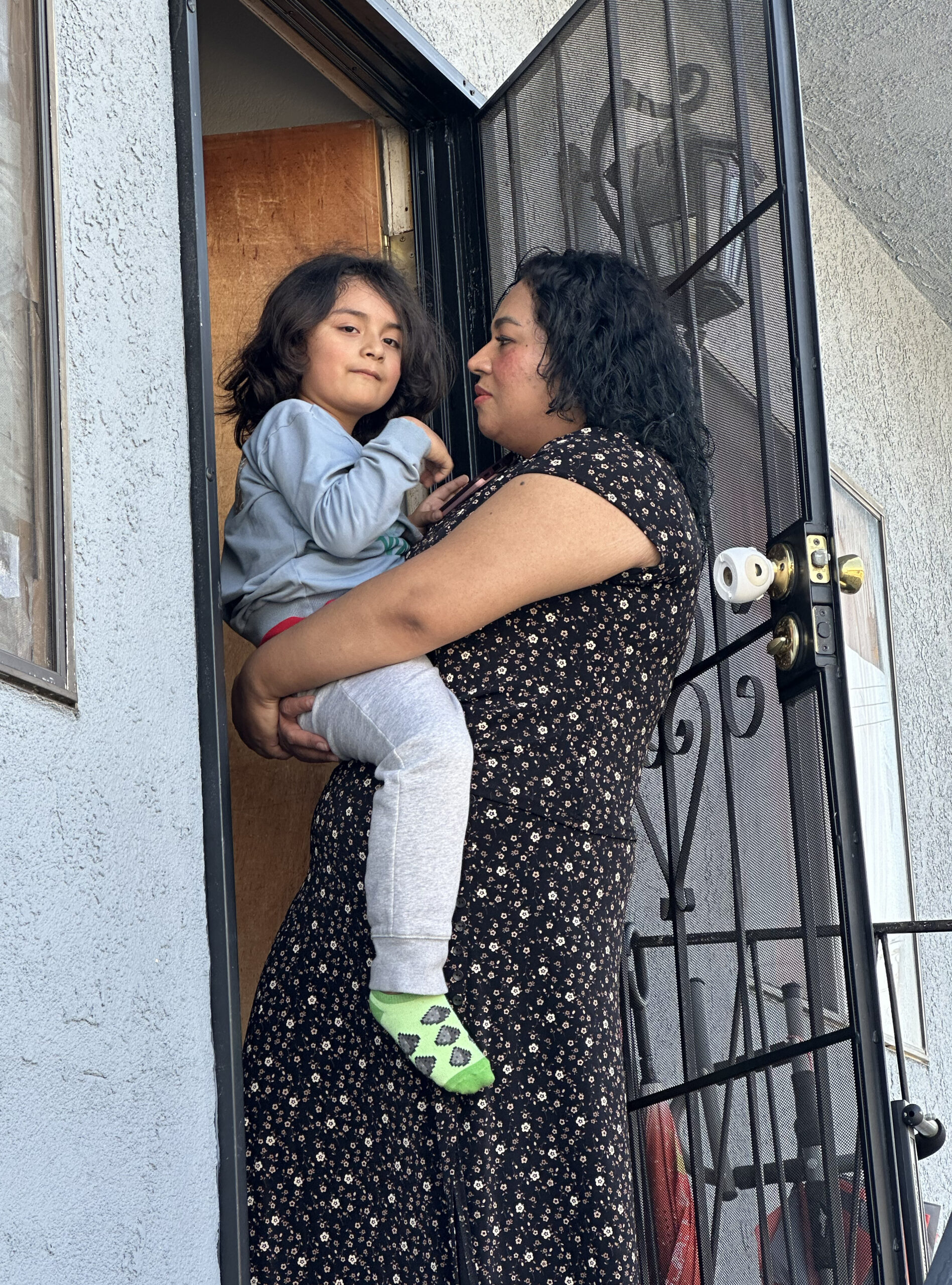 A mother holds her child in the front doorway of her Monterey Park home.