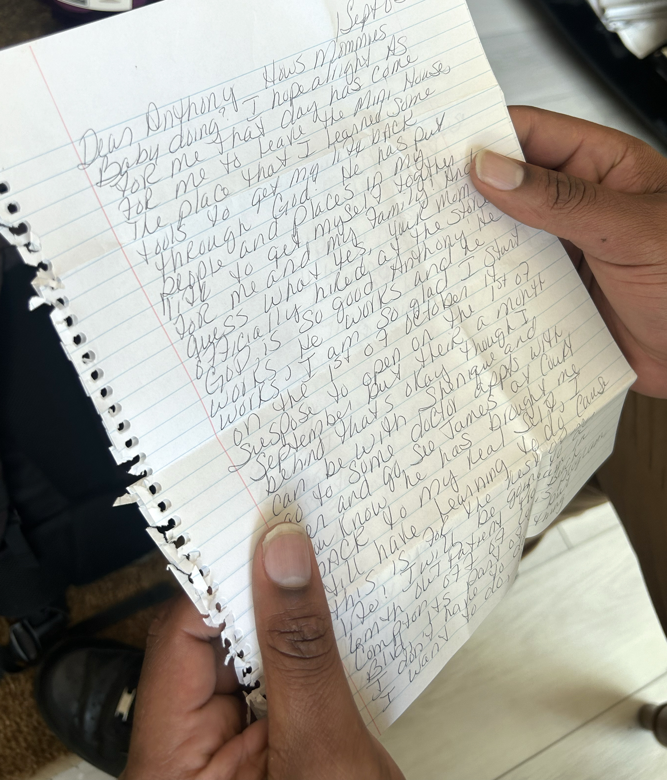 Black man’s hands hold a handwritten letter in pencil on lined notebook paper.