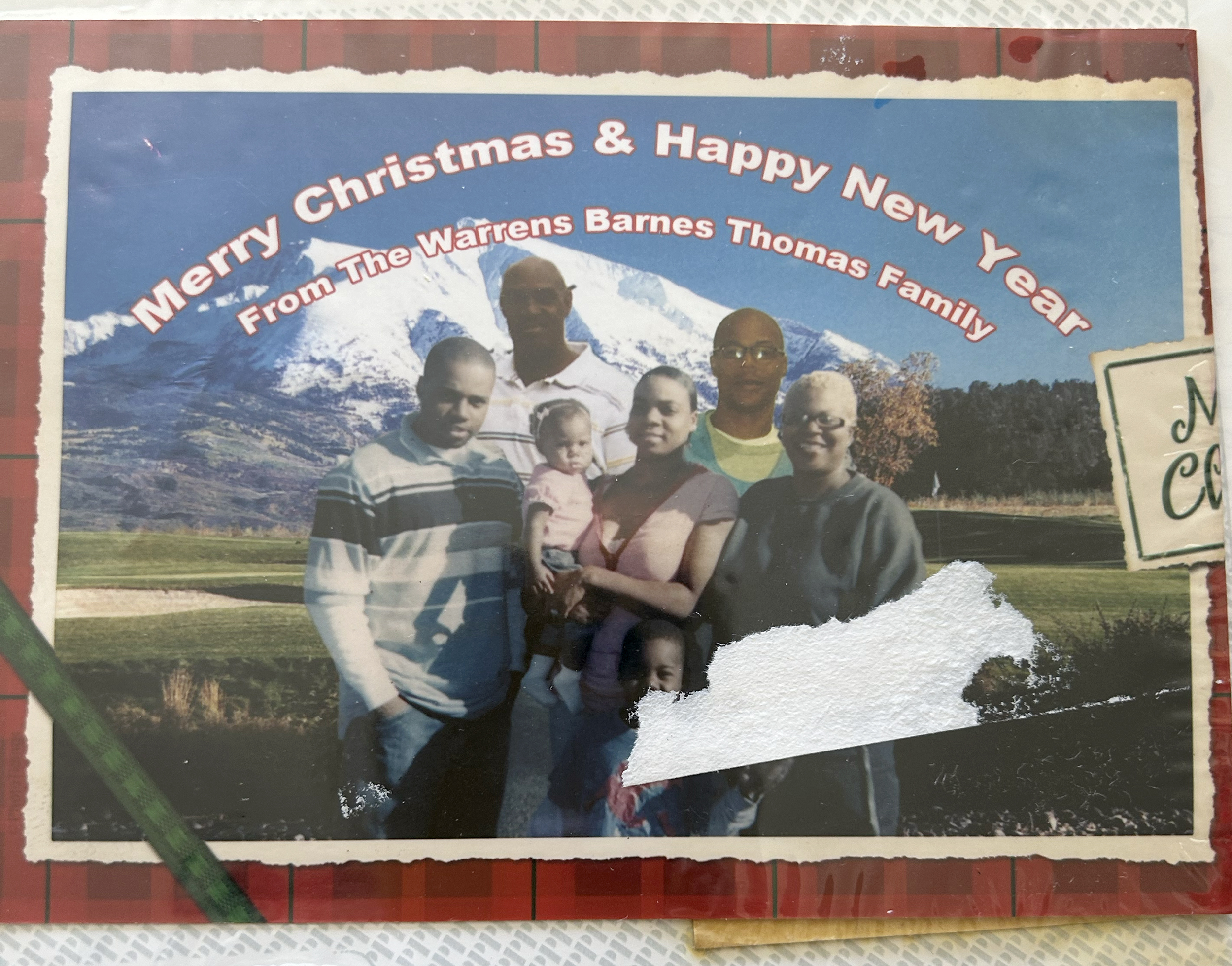 Five Black adults smile on the front of a Christmas card with a snowy mountain in the background. One of the adults, a woman, holds a baby in her arms with another at her hip.